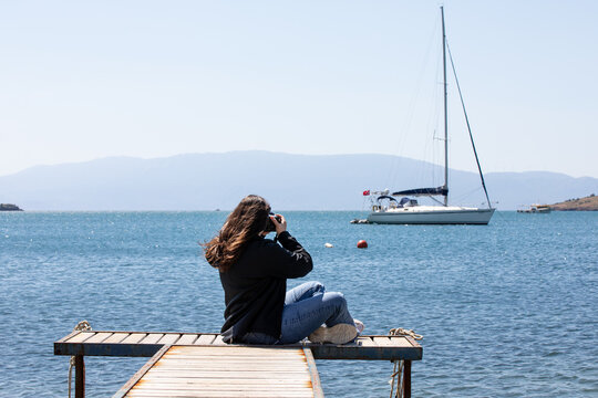 Young woman sitting on the pier and taking photos