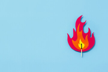 Fire made from multi-colored cardboard and match on blue background. Сoncept of careful handling...