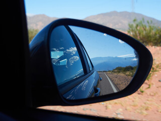 Route viewed through a rear-view mirror on the dessert in a sunny day