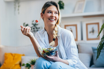 Smiling woman eating healthy salad while sitting on the kitchen at home.
