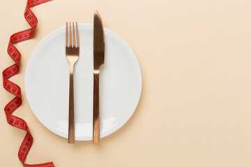 Measuring tape with empty plate on color background, top, view. Weight loss concept