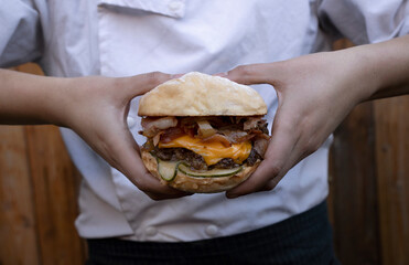 Caucasian female chef holding a monster burger with her hands. Layers of bread, meat, cheddar...