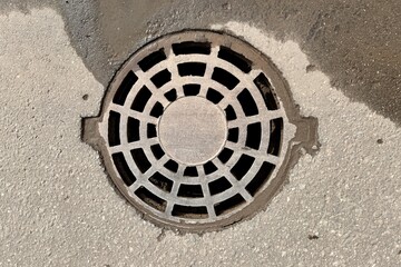 A iron hatch with a pattern above an observation well is located on auto road in daytime. Close-up