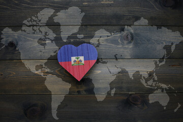 wooden heart with national flag of haiti near world map on the wooden background.