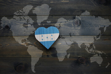wooden heart with national flag of honduras near world map on the wooden background.