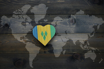 wooden heart with national flag of saint vincent and the grenadines near world map on the wooden background. - obrazy, fototapety, plakaty