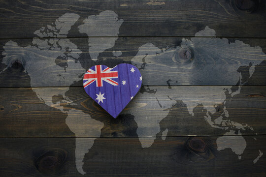 wooden heart with national flag of australia near world map on the wooden background.