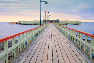 Pastel-colored bathhouse at the end of the wooden pier in dawn. The serene setting evokes peace and...