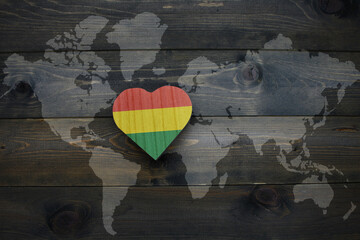 wooden heart with national flag of bolivia near world map on the wooden background.