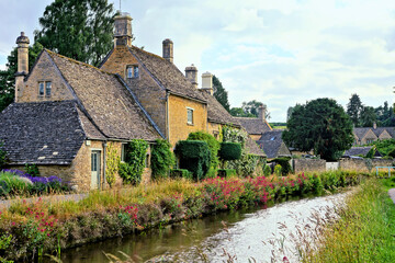 Cotswolds village of Lower Slaughter with flower lined river at dusk, Gloucestershire, England - 783410200