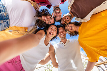 Group of young people taking a selfie standing in a circle outdoors. Youth community and friendship concept with diverse boys and girls laughing and celebrating together.