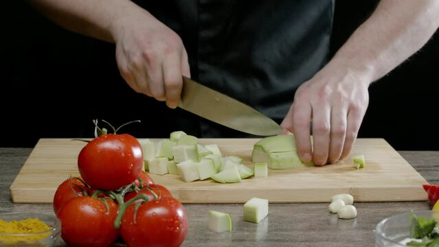 Man grinds a delicious fresh zucchini against a backdrop of other vegetables. He is preparing a vegetarian dish.