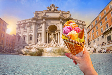 Italian bright sweet ice cream gelato cone with different flavors held in hand on the background of  famous Trevi Fountain in Rome, Italy - 783413411