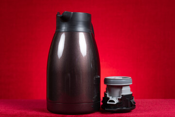 a stainless steel thermos bottle with the lid opened on red at horizontal composition