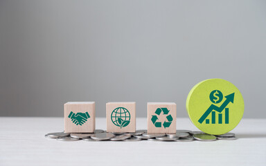 Eco business investment. Green icons on wooden cubes on money coin stack. Green business growth....
