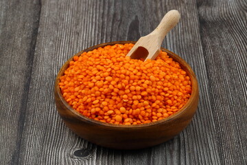 Red lentils in wooden bowl on wooden table background. Top view, copy space. Flat lay.