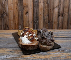 Gourmet sandwich. Closeup view of a grilled veal steak sandwich with fresh and grilles tomatoes, almonds and burrata cheese, with roasted potatoes as garnish, in a black dish on the wooden table.	
