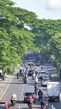 Vertical shot of cars, motorcycles, trucks, traveling through Jakarta's congested suburban roads in the morning. Depicts heavy traffic, pollution, and busy work