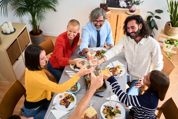 Top view of smiling Caucasian family at a meal together at home toasting with white wine and...
