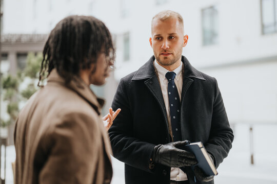 A focused image capturing a business discussion between two male people dressed in winter coats outside.