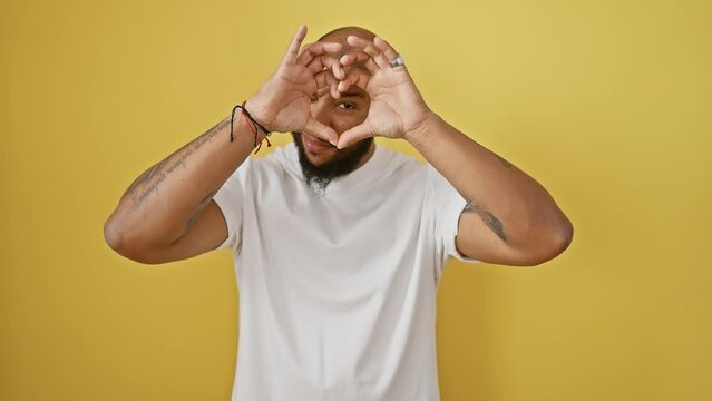 Smiling african american man in love, standing by yellow wall, making heart shape with hands, romantic concept