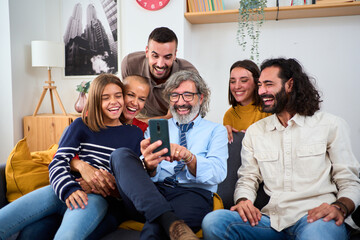 Caucasian multi-generational family gathered at living room sitting on sofa using mobile phone. Happy people smiling with a fun expression enjoying and watching funny videos together in cell at home