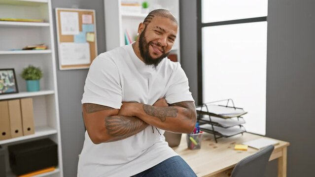 Confident bearded man in casual attire sitting at a modern workplace with arms crossed