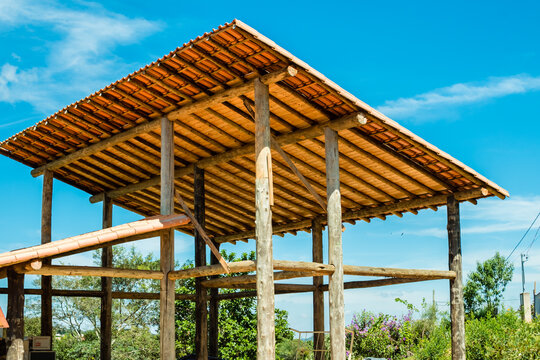 Work on the construction of a wooden building with round eucalyptus logs showing pillars, beams and roofs with tiles