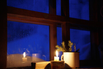 the light of the candle is reflected in the window behind which the winter evening is visible