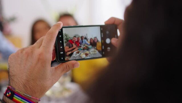 POV smart phone hold by caucasian man taking photo of reunion Caucasian family in celebration meal together indoors. Capture happy cell memories of people, 5g mobile or post on social networks