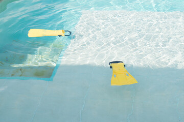 Yellow diving fins floating on blue pool water in sunny day 