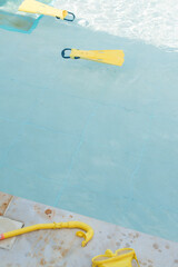 Vertical shot of yellow diving fins floating on blue pool water in sunny day, googles on pool edge