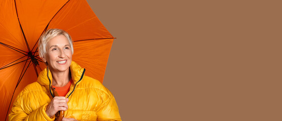 Beautiful mature woman with umbrella on brown background