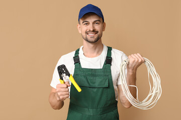 Portrait of male electrician with crimper and wires on beige background