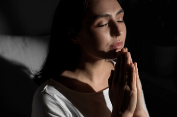 Young woman praying on dark background, closeup