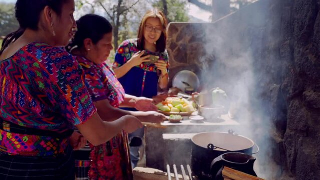 Two Latina women of the Mayan ethnic group cook and their daughter takes photos of them to share on social networks.