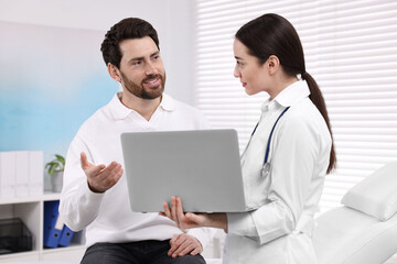 Doctor with laptop consulting patient during appointment in clinic