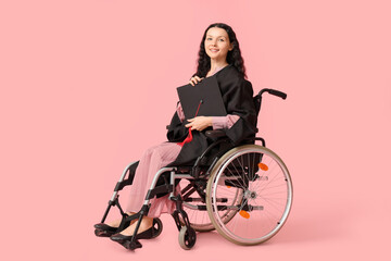 Beautiful female graduate student in wheelchair with graduation cap on pink background