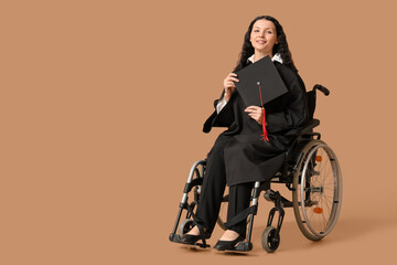 Beautiful female graduate student in wheelchair with graduation cap on brown background