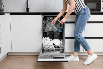 Woman loading dishwasher with glasses and plates in kitchen, closeup