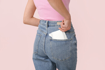 Woman putting menstrual pad into pocket on pink background