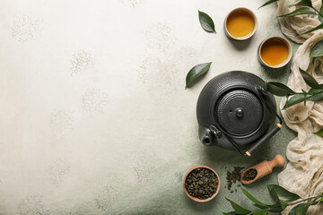 Teapot and cups of green tea with leaves on grey grunge background