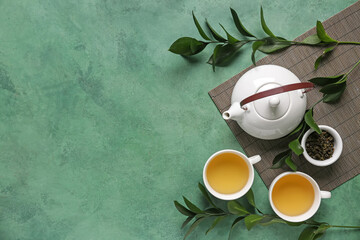 Teapot and cups of tea with leaves on green grunge background