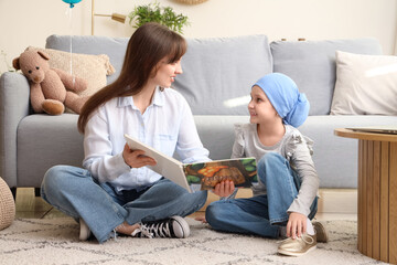 Little girl after chemotherapy with her mother reading story at home. International Childhood...