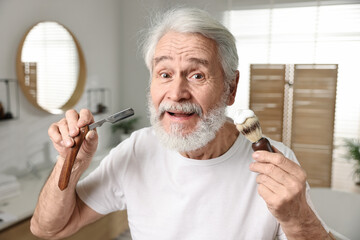 Man shaving mustache and beard with blade in bathroom