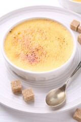 Delicious creme brulee in bowl, sugar cubes and spoon on white table