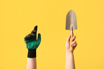 Female hands with glove and gardening shovel on yellow background, closeup