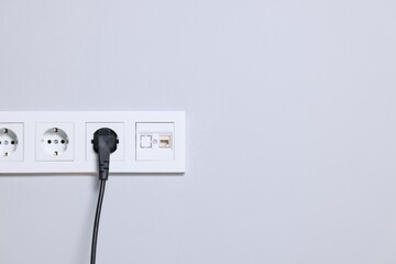 Power sockets and electric plug on grey wall, space for text