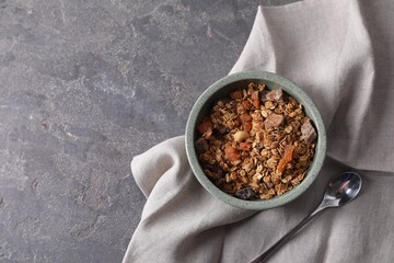 Tasty granola in bowl, spoon and napkin on gray textured table, flat lay. Space for text