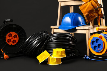 Stepladder with hardhat, rolled wires, extension cable reels and electrical junction boxes on black background - 783449650
